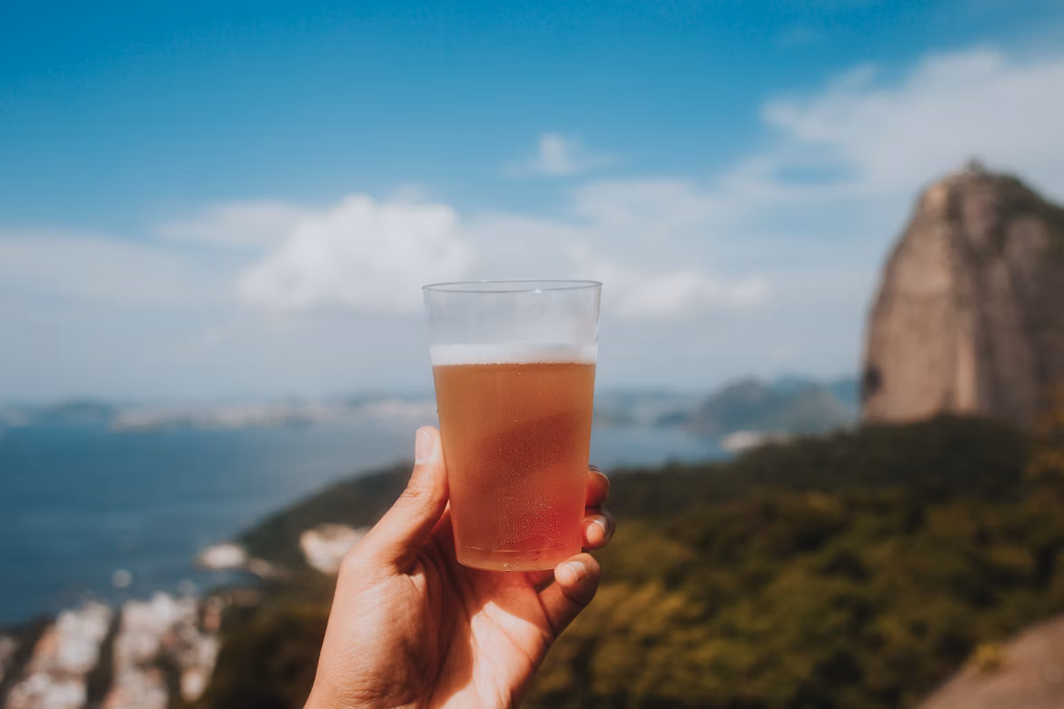 Pessoa segurando um copo a frente de uma paisagem - Foto: Freepik