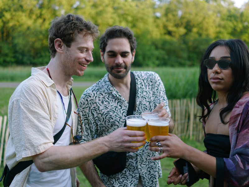 três jovens brindando estilos de cerveja refrescantes para o verão em copos de plástico transparente