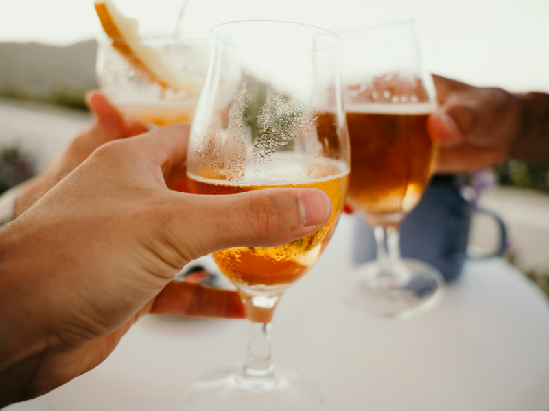 três pessoas brindando estilos de cerveja refrescantes para o verão em taças de vidro ao ar livre