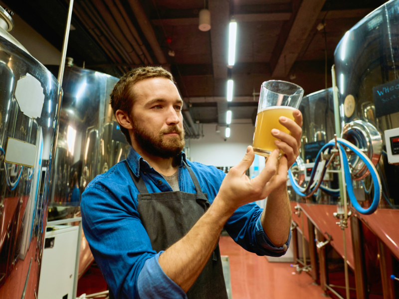 funcionário de avental de uma das cervejarias pelo mundo analisando a cor de uma cerveja no copo