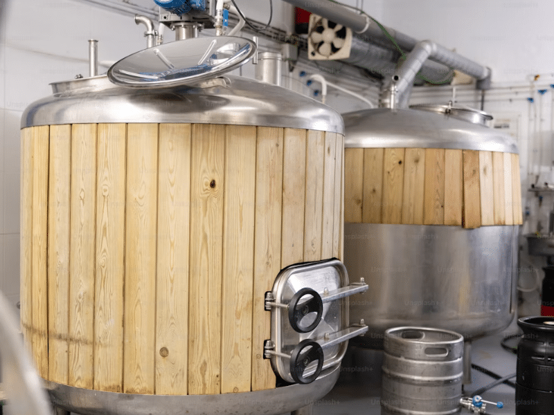 Alt Text (Sucinto):
Dois grandes tanques de fermentação de cerveja, combinando aço inoxidável e revestimento de madeira vertical, em uma cervejaria moderna.